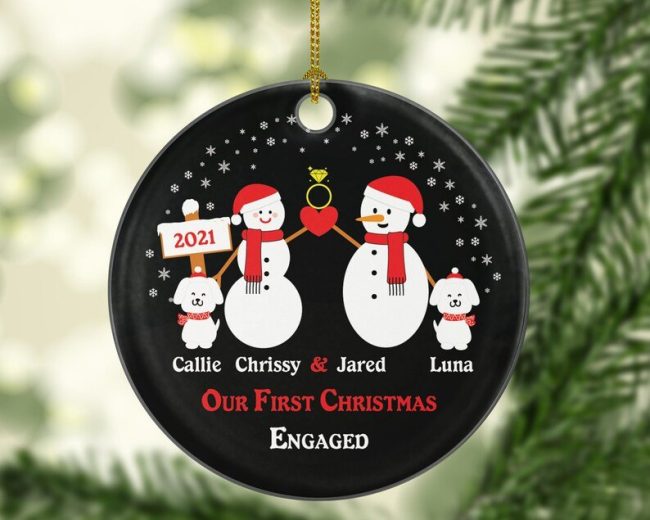 Black round ornament with a snowman couple, a ring and two small dogs above sample names and Our First Christmas Engaged