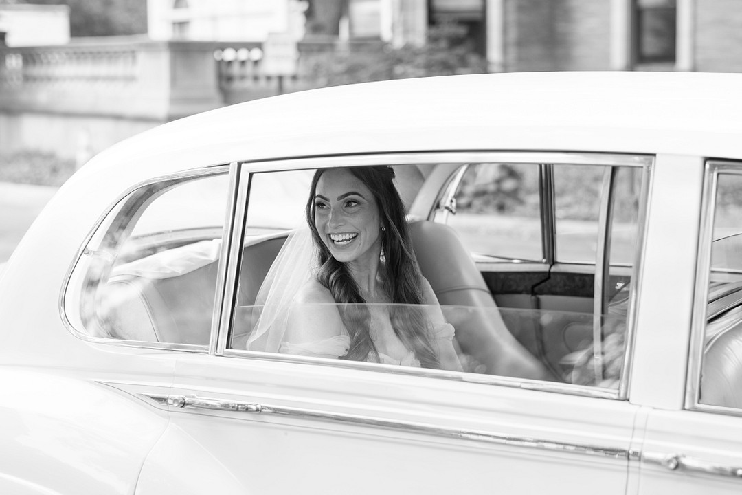 Bride smiling from the back seat of a vintage white car