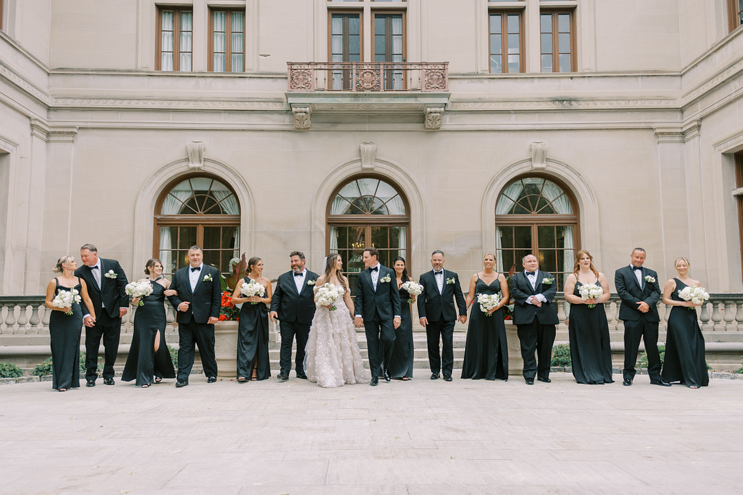 Wedding party in black lined up in front of a stone mansion