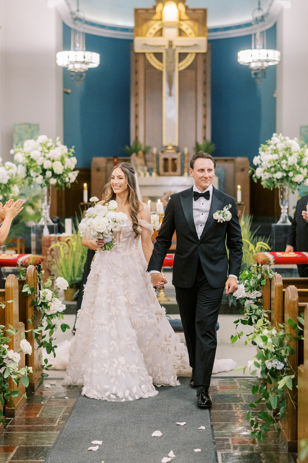 Bride and groom walking up the church aisle lined with white flowers