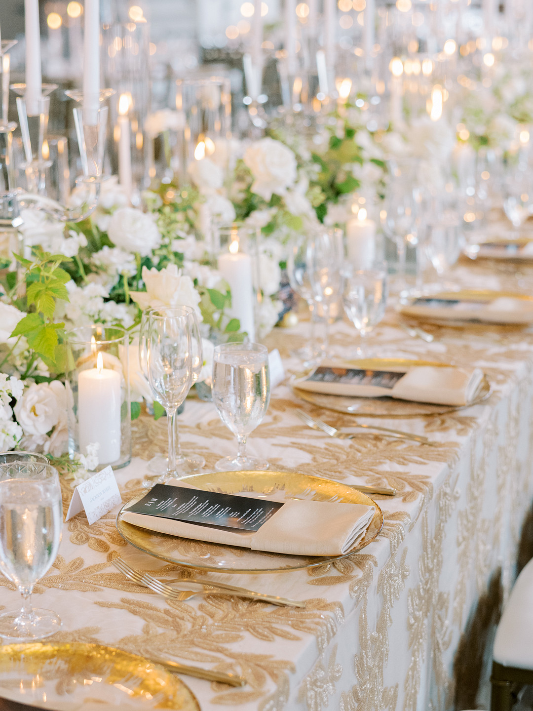 Long reception table set with gold chargers, candles and tall white arrangements