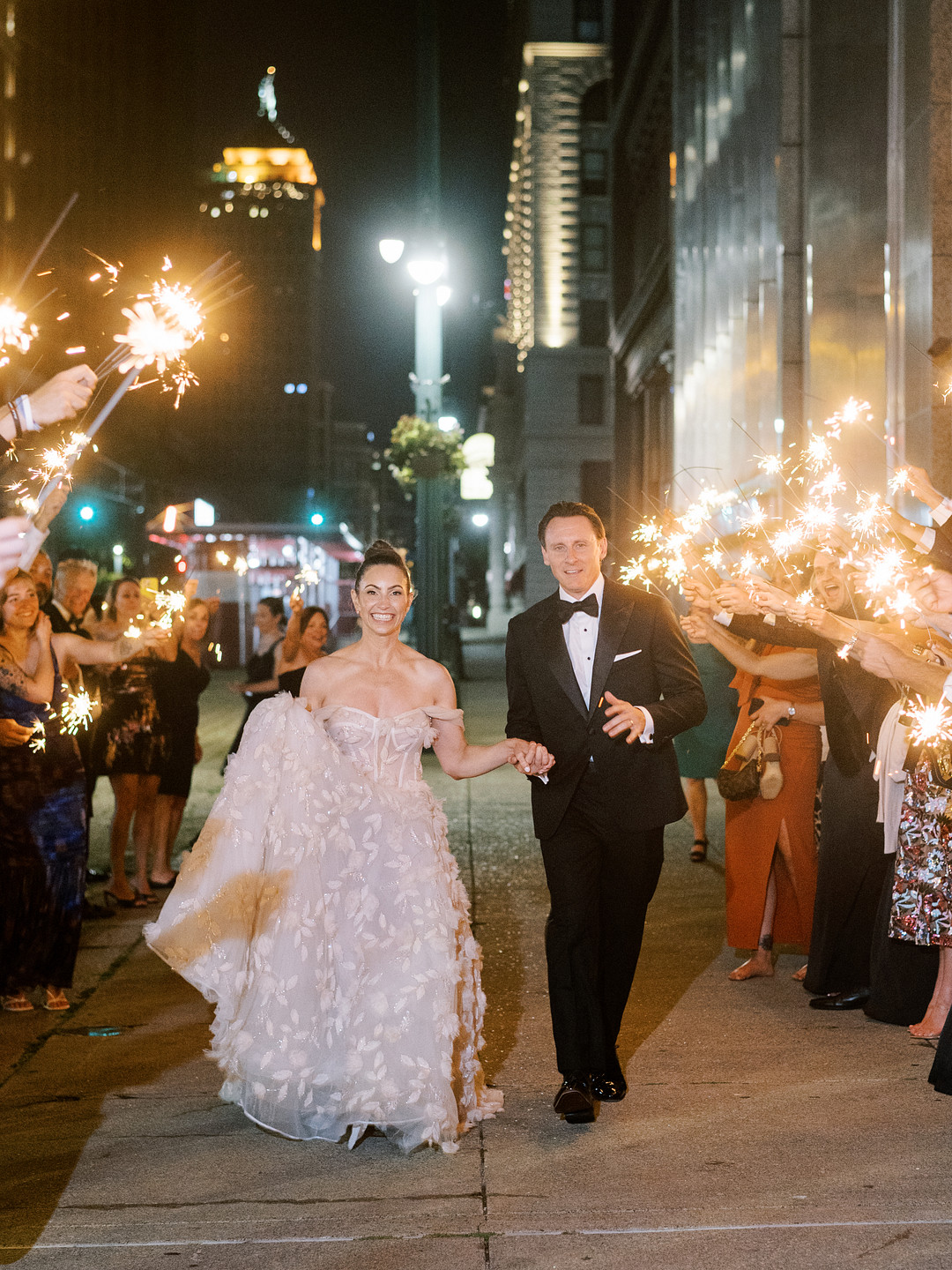 Bride and groom walking out at night as guests cheer