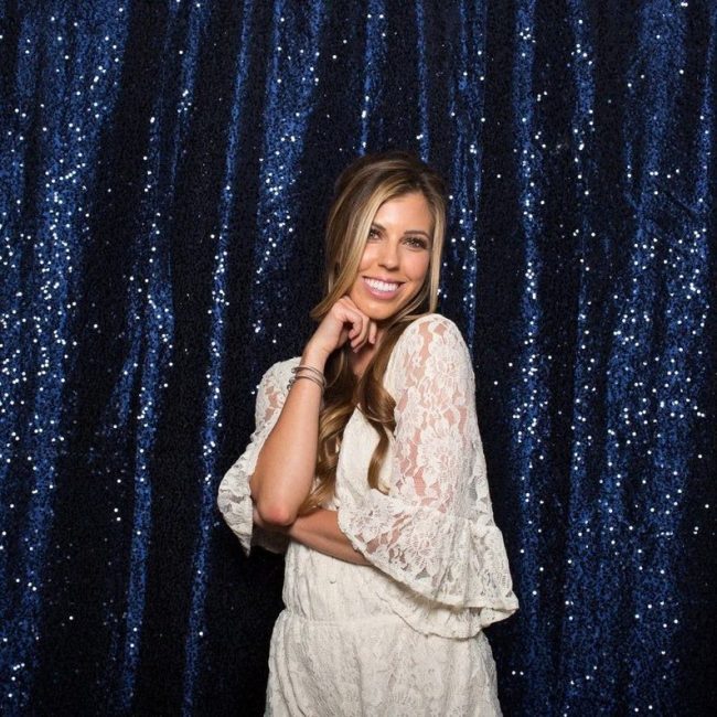 Woman in a white lace dress posing in front of an aklinens navy sequin photo backdrop