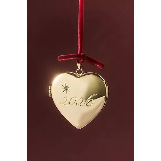 Anthropologie gold heart locket ornament engraved with 2026, hanging from a red velvet ribbon tied in a bow