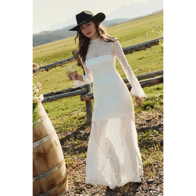 Model in a field wearing the BHLDN long-sleeve white lace maxi dress with a high neck