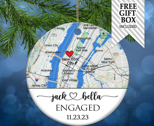 White porcelain ornament with a New York City map, a red heart marking the spot, and sample names above Engaged and a date