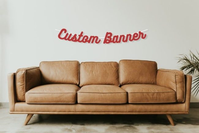 CutAndCreateCo red script banner reading Custom Banner hung on a wall above a leather sofa