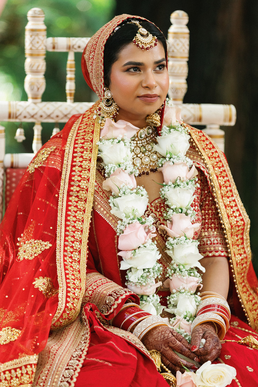 Bride in red with a white flower garland during the ceremony