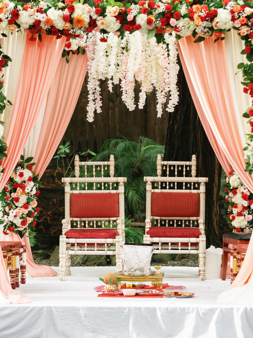 Mandap with red and gold chairs, blush draping and red and white flowers at Deer Park Villa