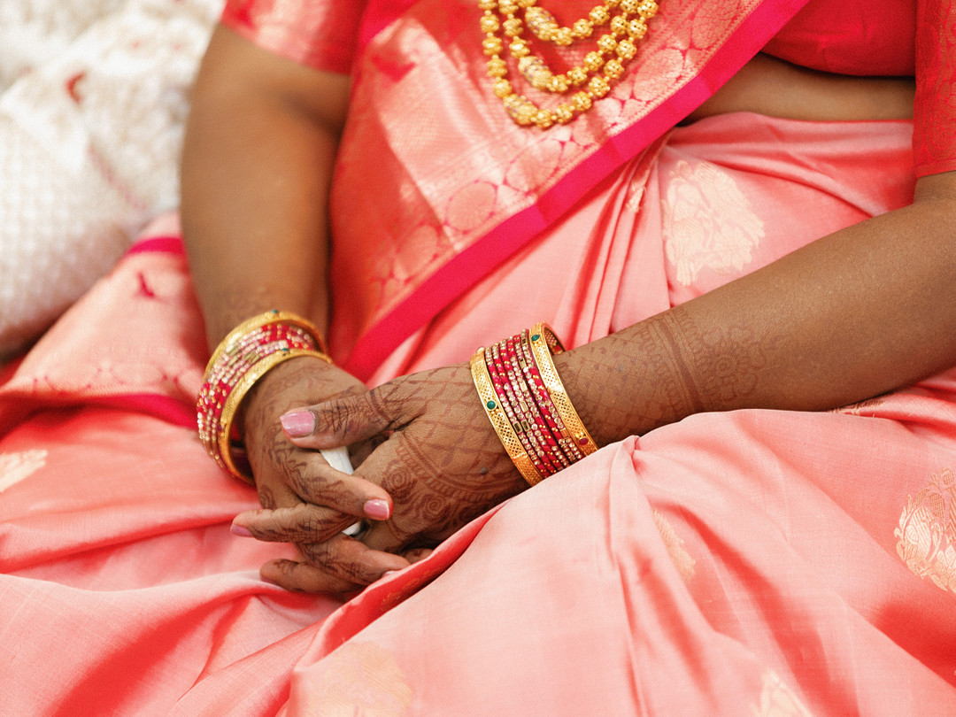 Hands with henna and gold bangles resting on a coral sari