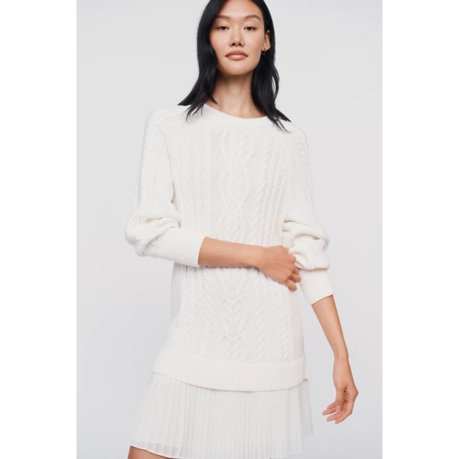 Model in the Delphine twofer mini dress, an ivory cable-knit sweater layered over a pleated skirt