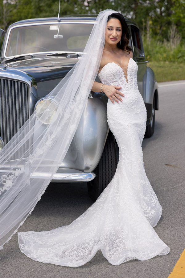 Bride leaning on a vintage silver car with her veil draped over it