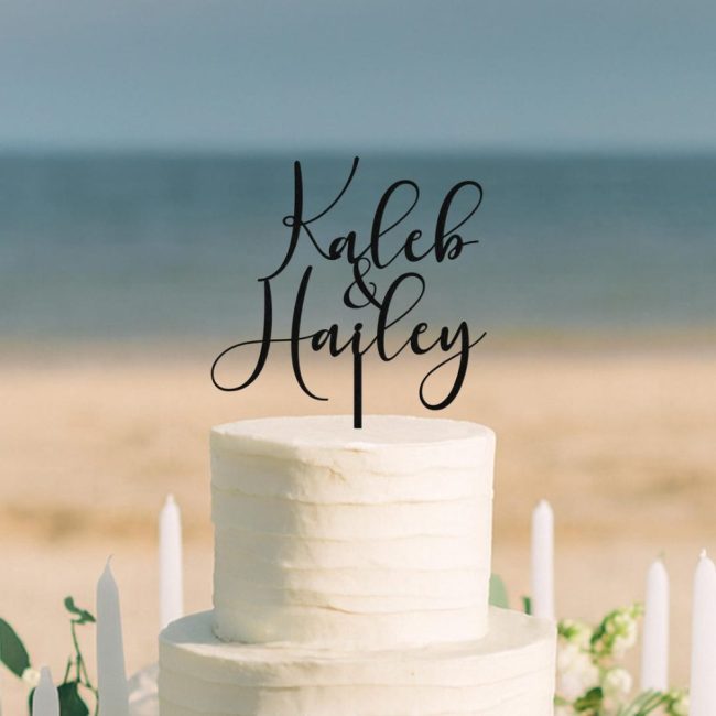 EndIessCreationsCo black acrylic cake topper with Kaleb and Hayley in script on a white cake at the beach