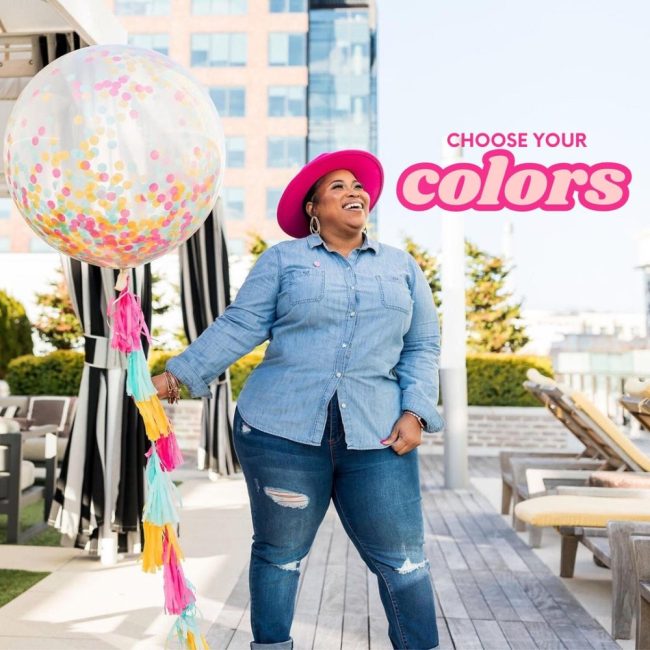 Woman holding a GlamfettiCo jumbo clear confetti balloon with a colorful tassel tail on a rooftop
