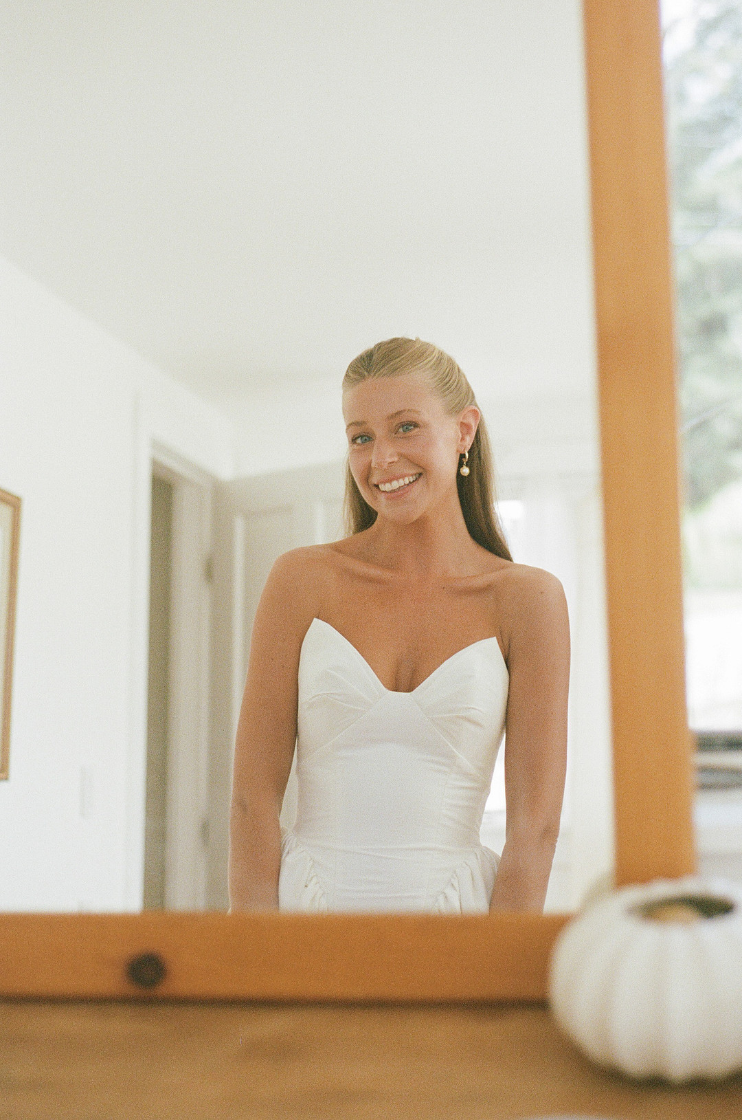 Bride smiling into a mirror in her strapless linen ballgown