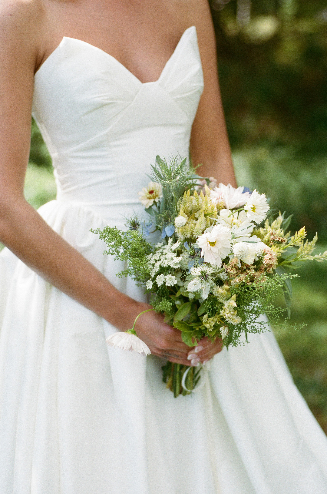 Bride holding a bouquet of white and blue flowers and greenery