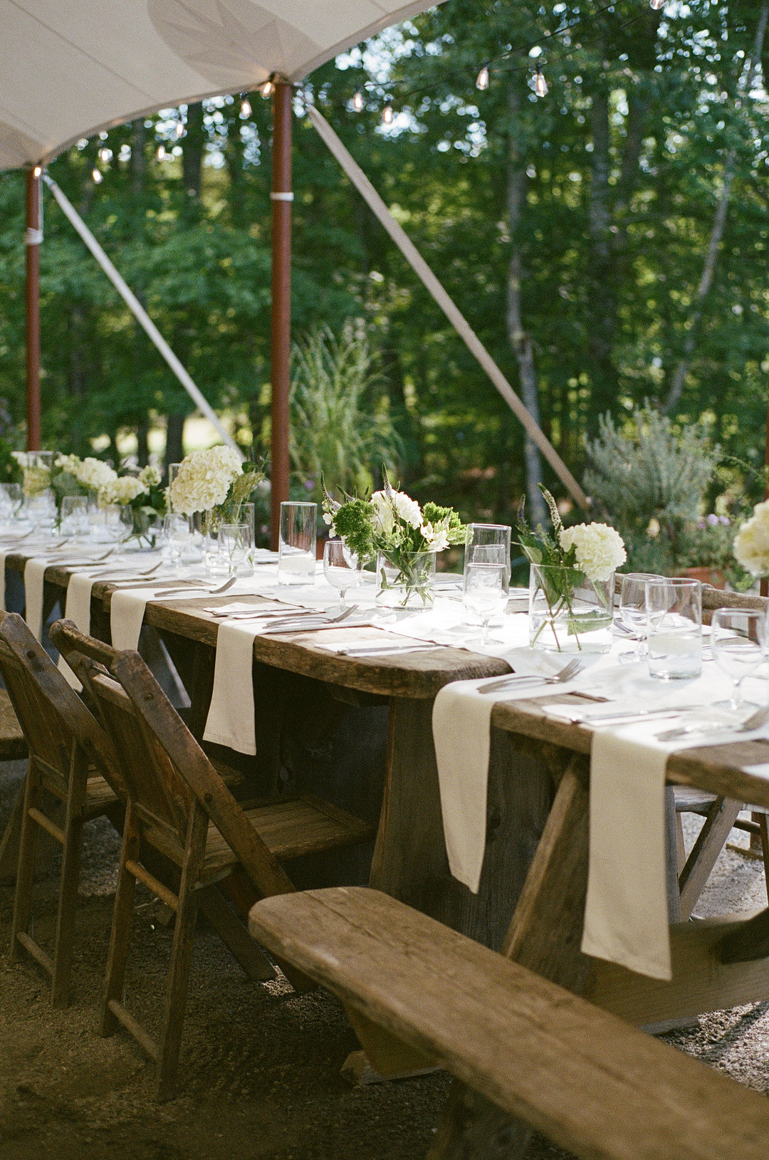 Long wooden tables set with white linens in the reception tent
