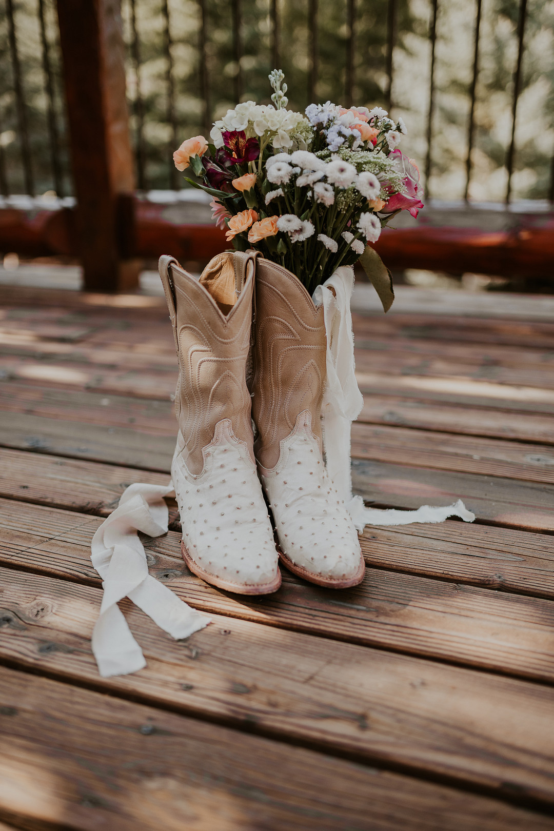 White cowboy boots and a colorful bouquet on a wooden deck