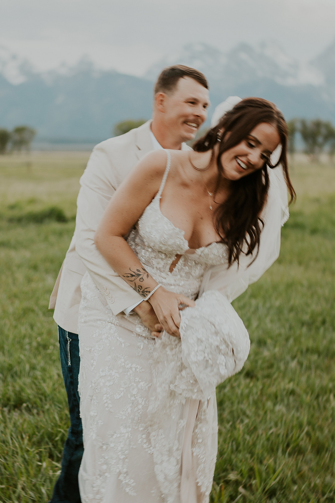 Groom laughing as he hugs the bride in a meadow