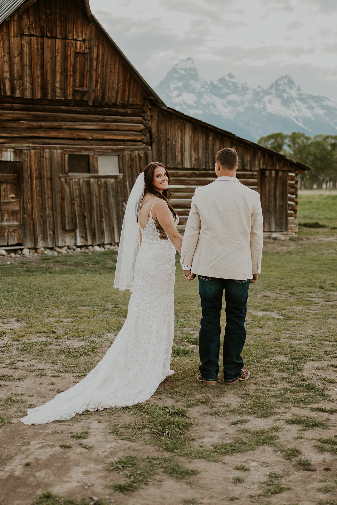 Bride and groom walking toward a weathered wooden barn below the Tetons