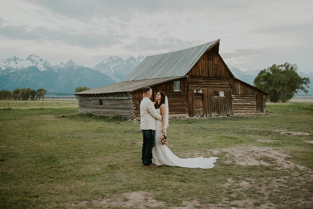 Bride and groom in a field in front of a wooden barn and the Teton Range