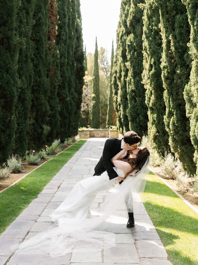 Groom dipping the bride in the cypress-lined walkway