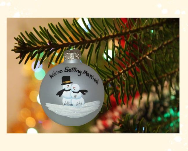 Glass ball ornament hand-painted with two snowmen and sample names, hanging on a Christmas tree