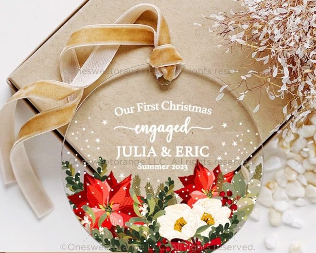 Clear glass ornament with red poinsettias and white flowers around Our First Christmas engaged and sample names