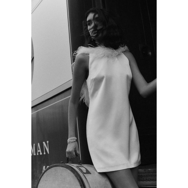 Black-and-white photo of a model in the Hutch high-neck mini dress with feather trim at the neckline