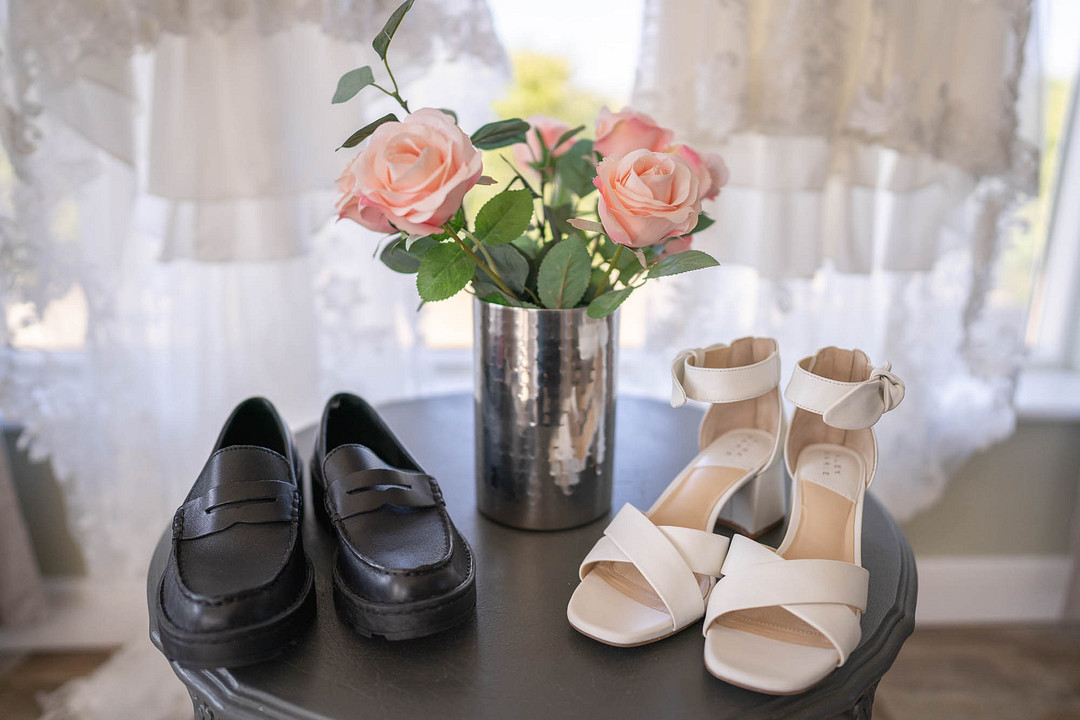 Two pairs of wedding shoes and pink roses by a window
