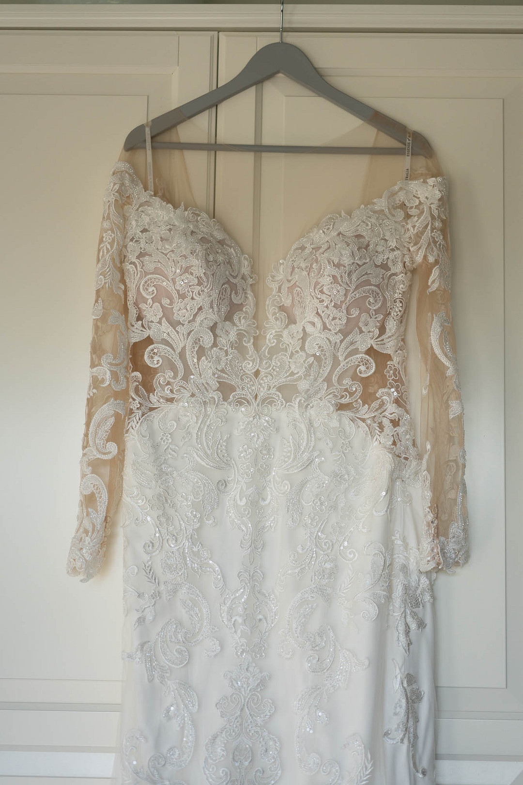 Lace wedding gown with sheer sleeves hanging by a window