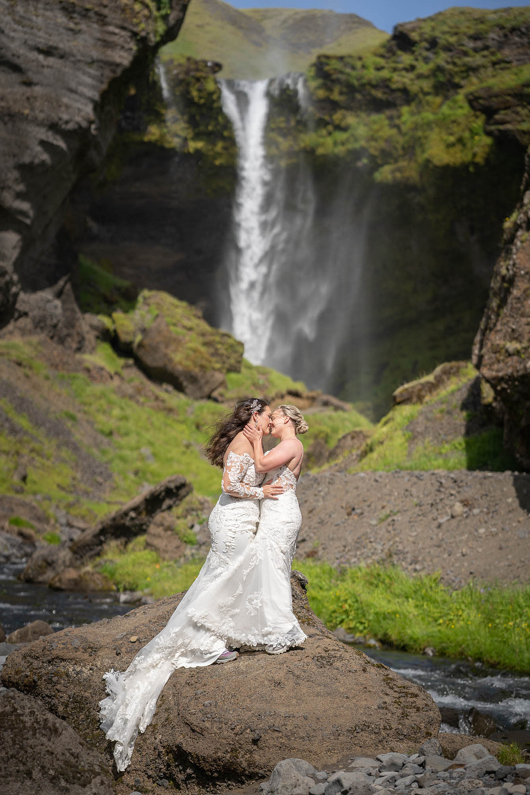 Posing in a wedding gown on a mossy rock in front of a waterfall