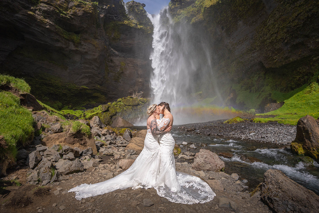 The couple kissing in front of a tall waterfall