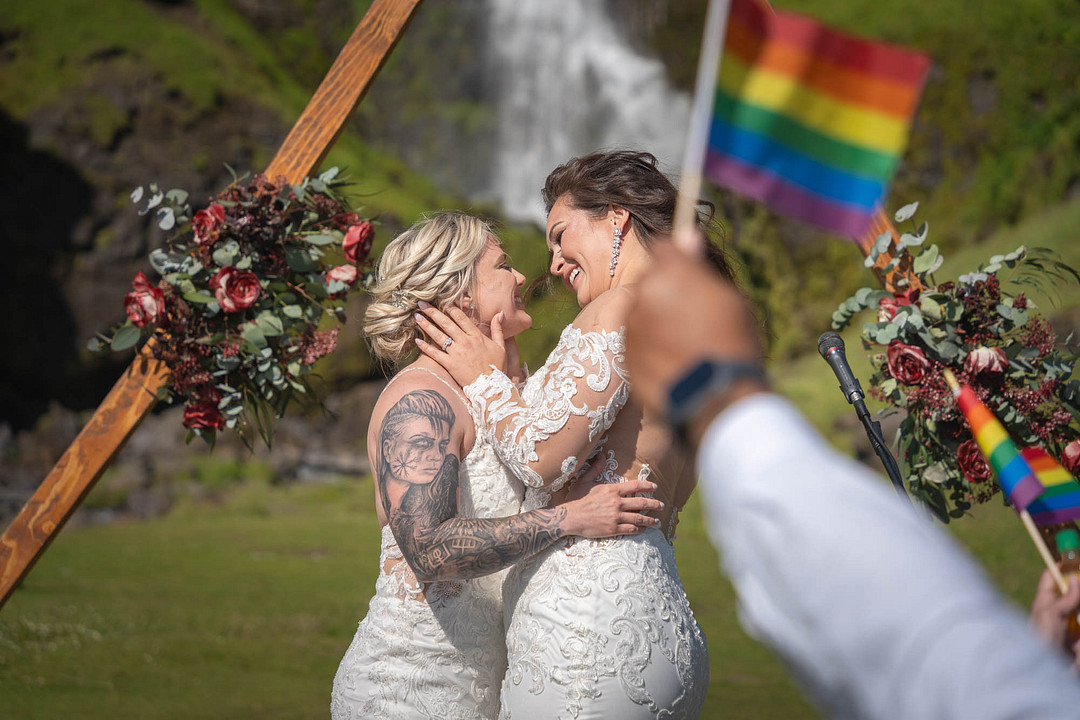 The couple kissing as a guest waves a rainbow flag