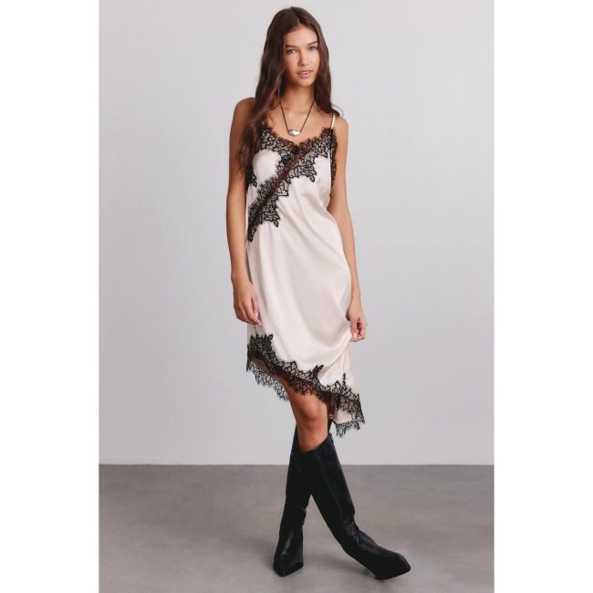Model in the Kimchi Blue Cross My Heart ivory satin midi slip dress with black lace trim and an asymmetric hem, worn with black boots