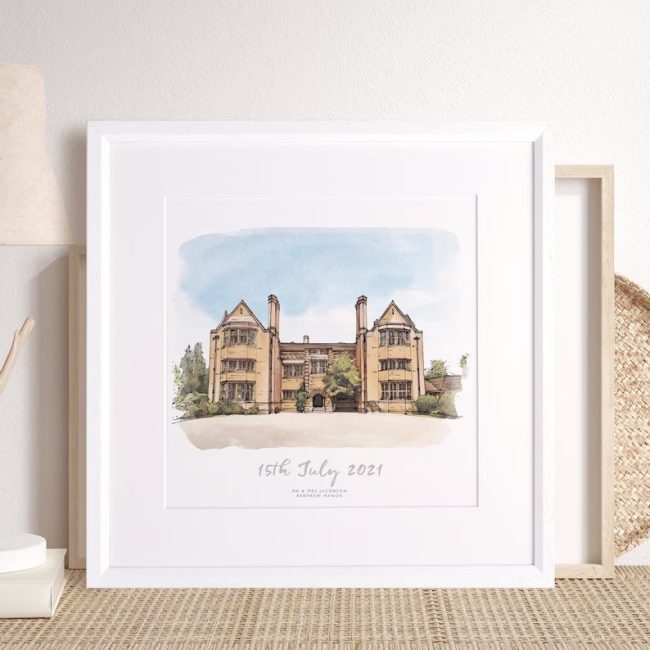 Framed watercolor sketch of a stone manor house wedding venue with the wedding date written below, in a white frame