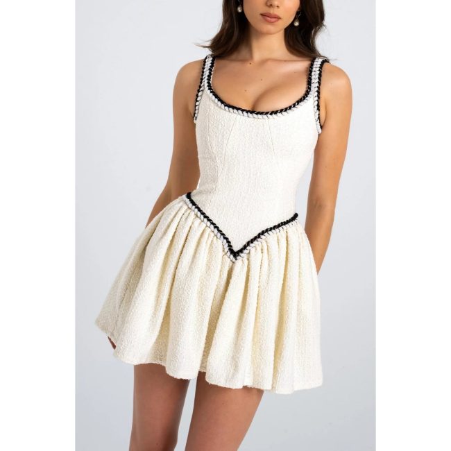 Model in the Miss Circle Coco ivory boucle tweed mini dress with black pearl-edged trim and a pleated skirt
