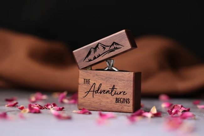 NorthStarEngraving slim walnut ring box engraved with mountains and The Adventure Begins, standing open