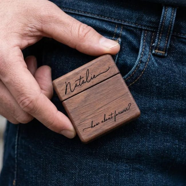 Hand slipping an OHCgifts slim walnut ring box engraved with a name in script into a jeans pocket