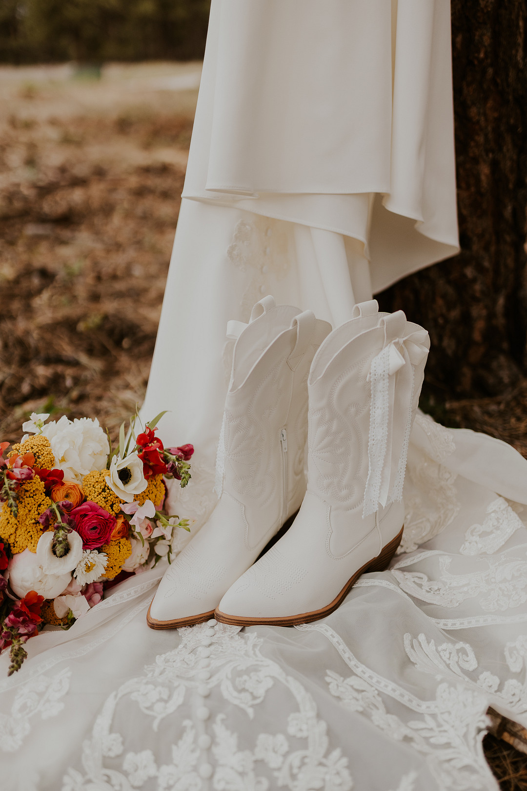 Wedding gown hanging from a tree with white cowboy boots and a bright bouquet