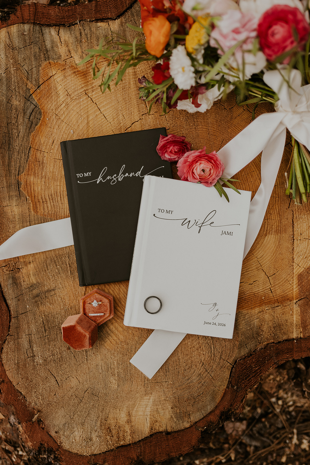 Invitation and vow cards on a wood slice with orange and red flowers