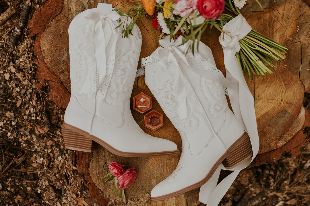 White cowboy boots on a wood slice beside a bright bouquet