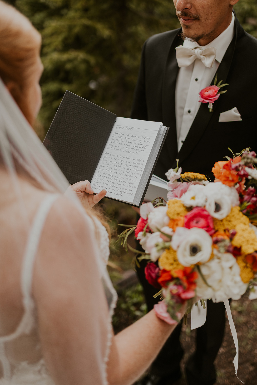 Bride reading her vows while holding an orange, red and white bouquet