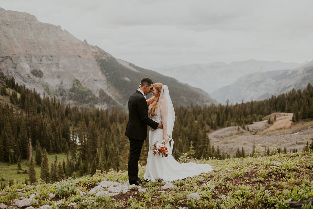 Bride and groom on a ridge overlooking a mountain valley near Ouray