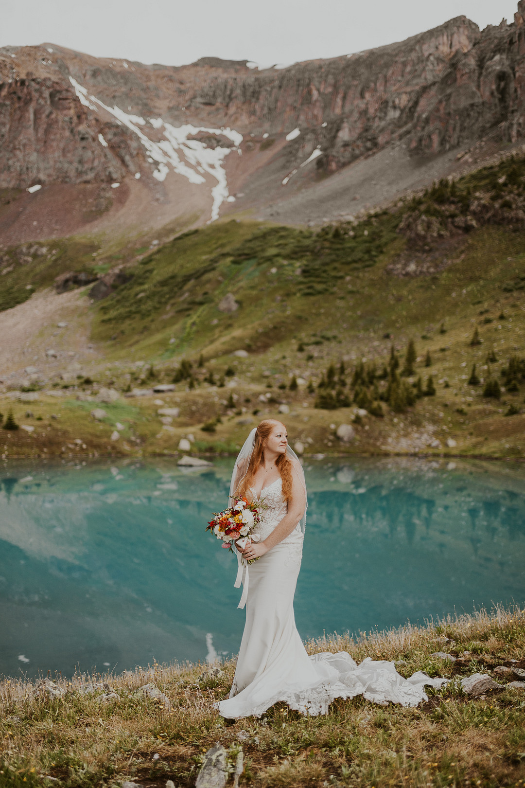 Bride in her gown above a turquoise alpine lake in the San Juan Mountains