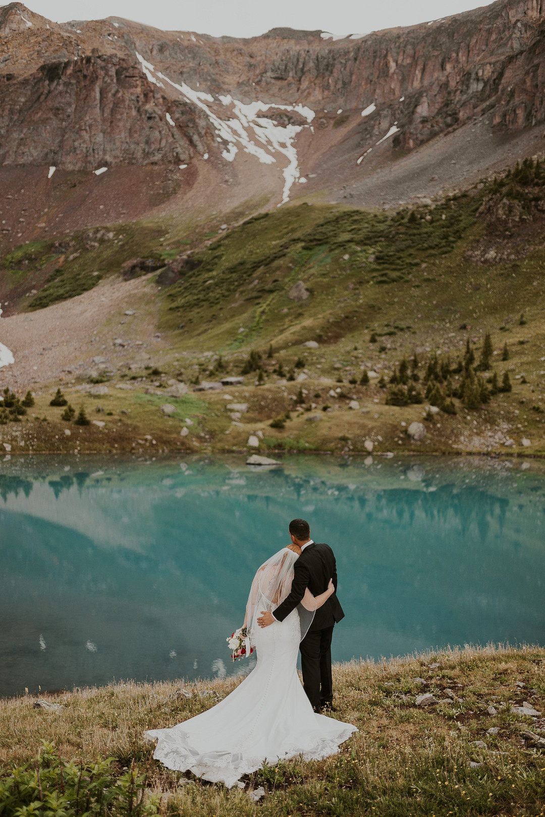 Couple embracing on the shore of a turquoise lake below rocky peaks