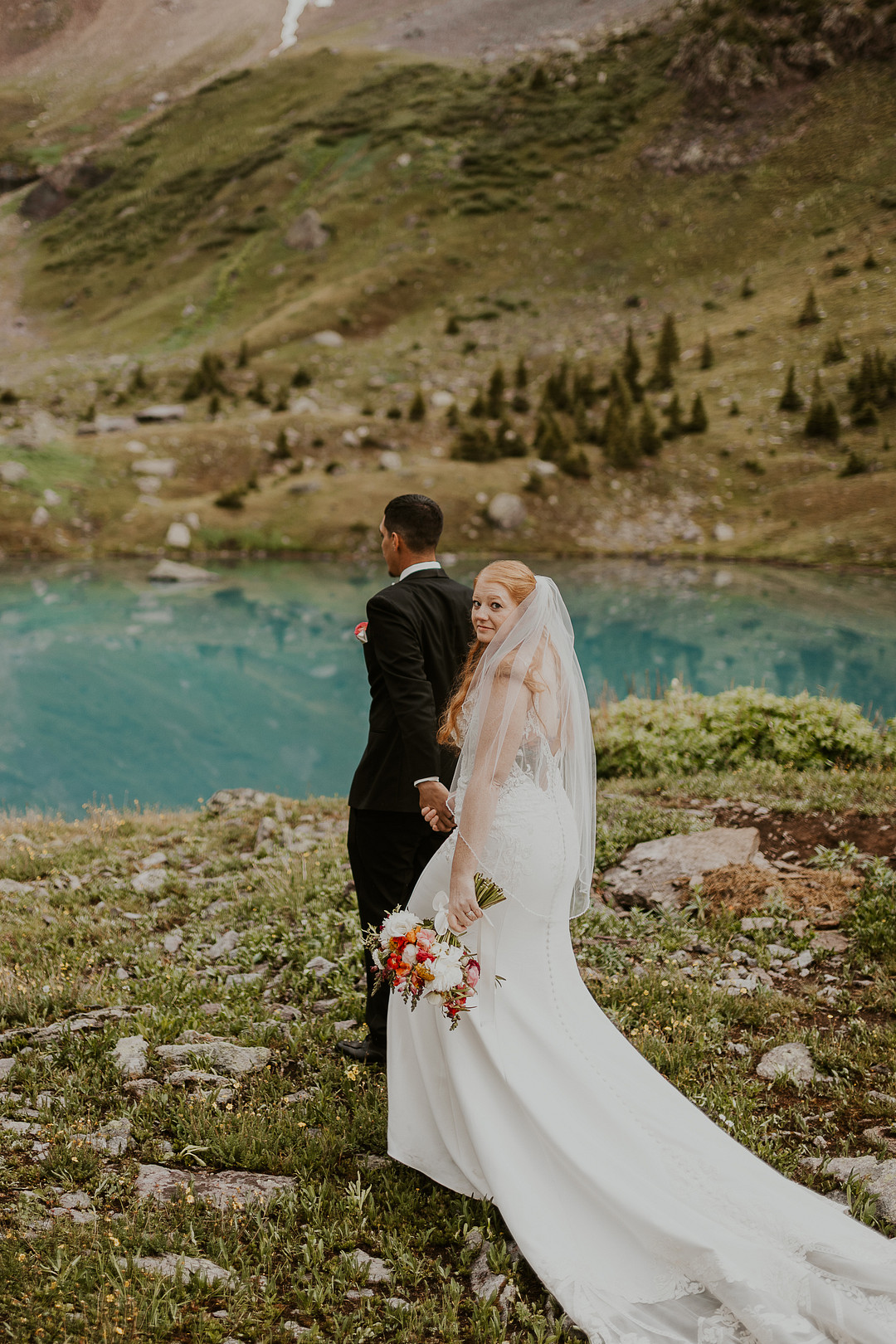Bride and groom on a grassy slope above an alpine lake