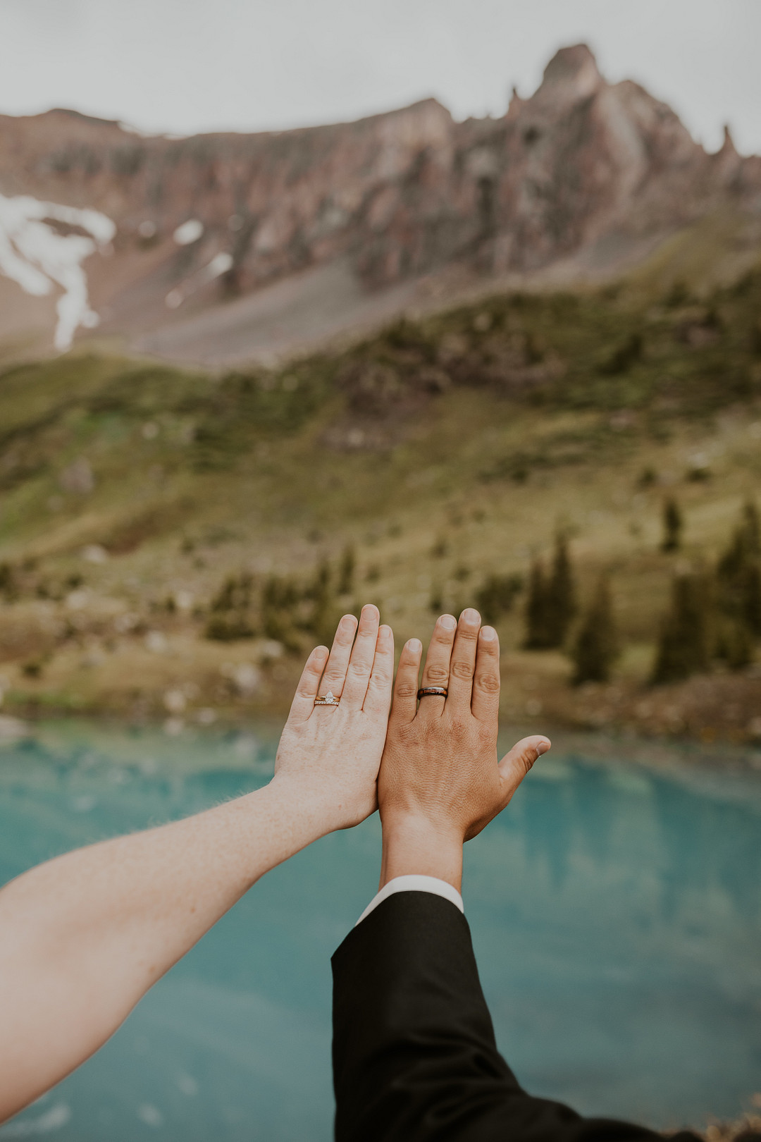 Bride and groom reaching for each other's hands with the mountains and lake behind them