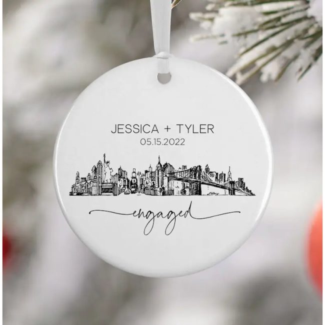 White round ceramic ornament printed with a black New York City skyline, sample names, a date and engaged in script