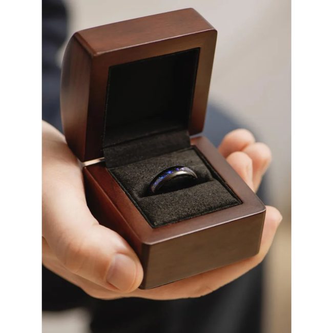 Hand holding an open RedwoodRings walnut ring box with a dark band in the black lining